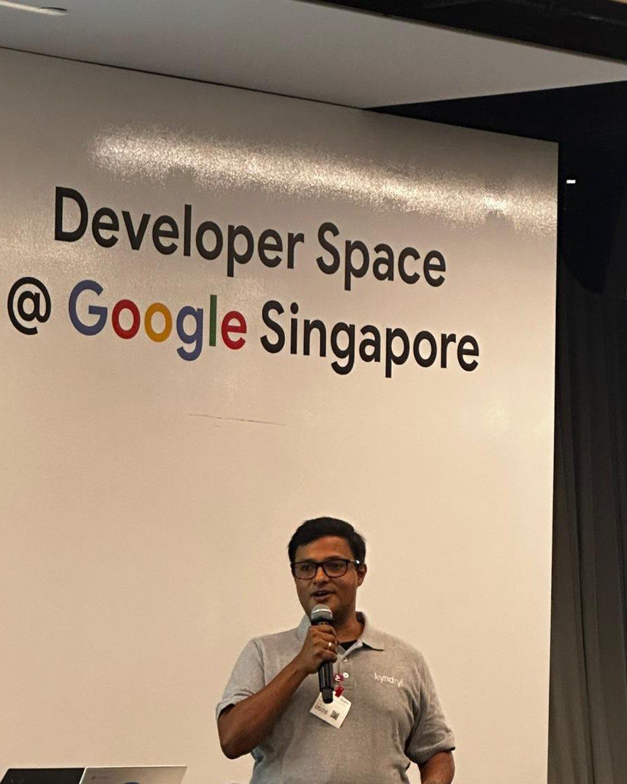 Vishnu Nanduri speaking with a microphone in front of a Developer Space at Google Singapore sign