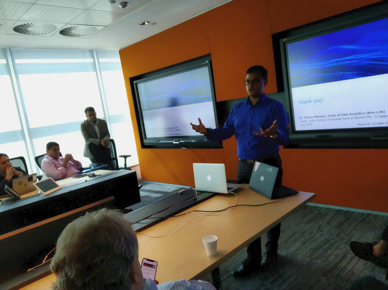 Vishnu Nanduri presenting in a meeting room in front of a screen showing a thank-you slide