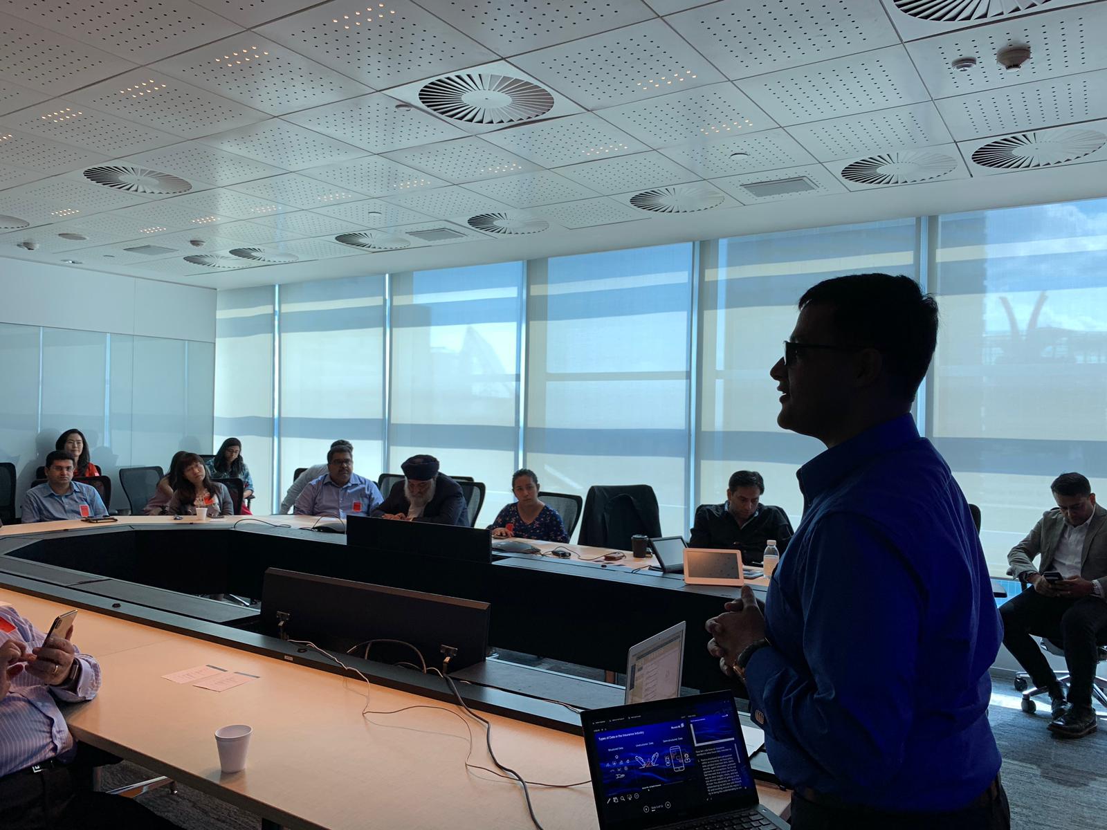Vishnu Nanduri presenting to an audience seated around a conference table